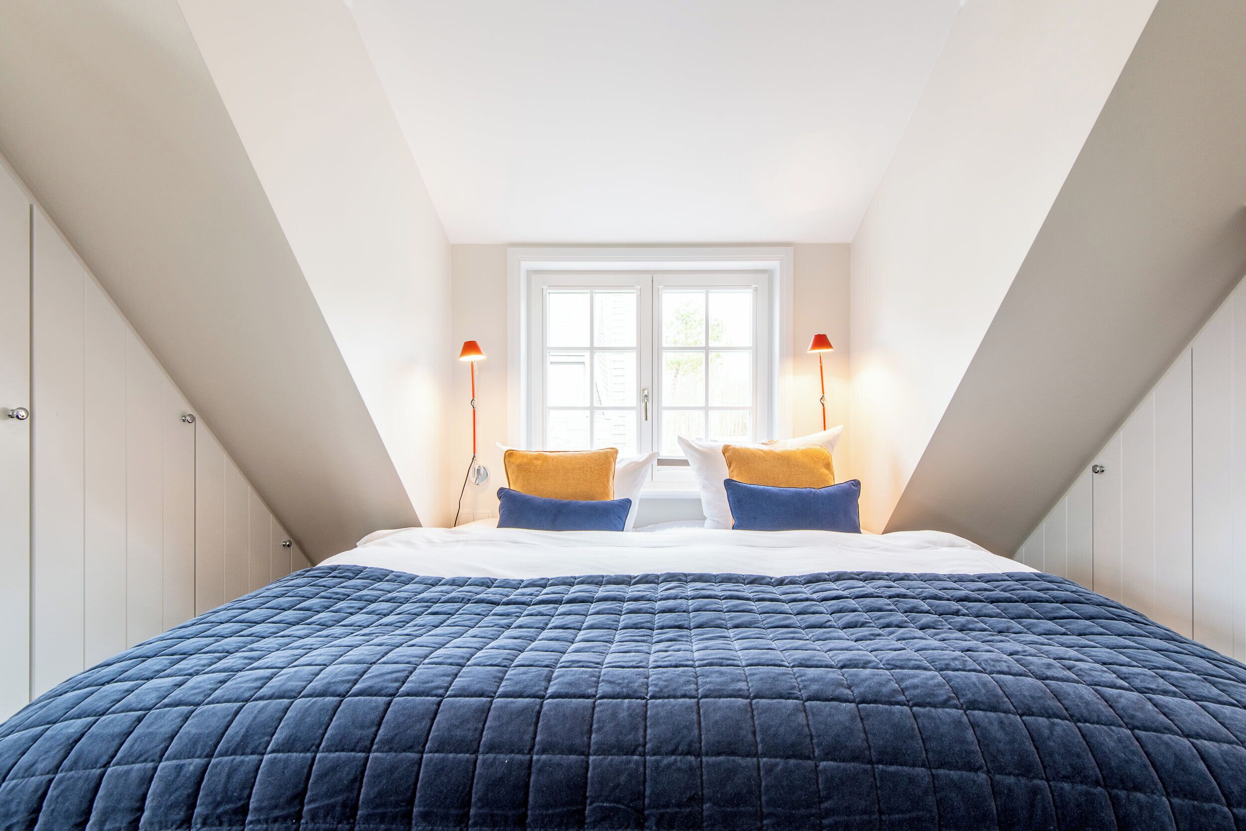 A bedroom with a large bed, two bedside lamps, and a window with a view.