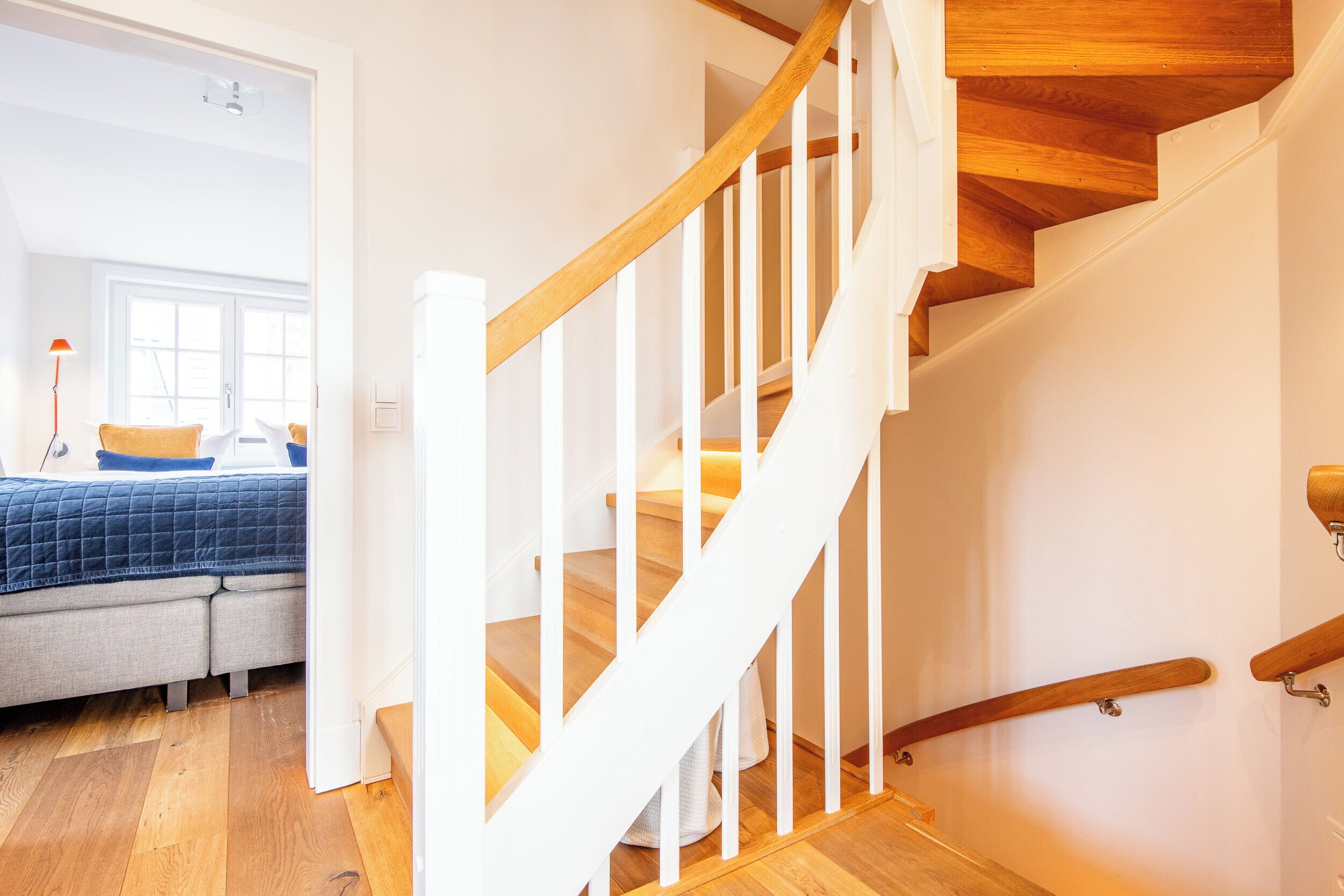 A staircase with wooden steps and white railings, leading to a room with a bed and a window.