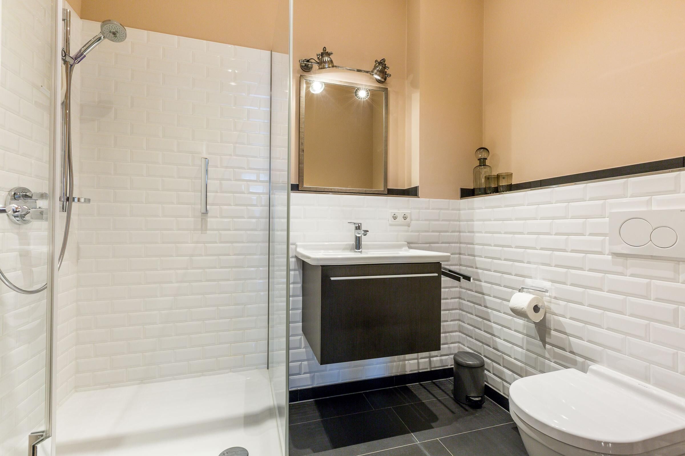 Een moderne badkamer met een douchecabine van glas, een witte wastafel met een donker kastje, en een toilet.