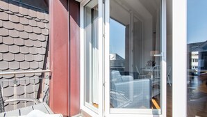Ein Balkon mit einer Glastür, die zu einem Innenraum mit gemusterten Stühlen und einem Tisch führt.