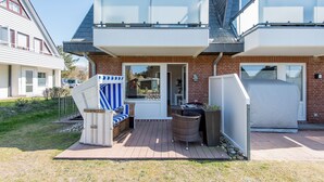 Ein zweistöckiges Haus mit einem Balkon, einer überdachten Sitzterrasse und einem Garten.