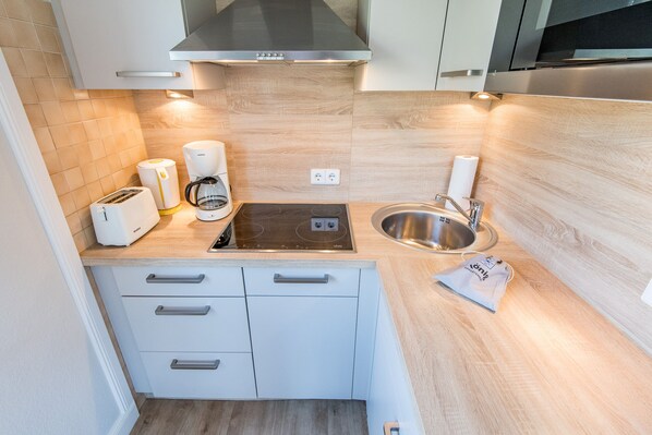 A compact kitchen with a built-in stove, a sink, and a coffee maker.