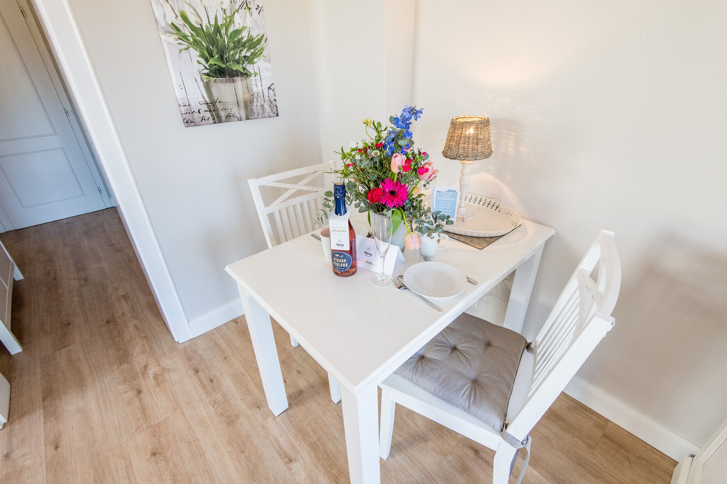 Une table à manger recouverte d’une nappe blanche, un vase rempli de fleurs, une bouteille de vin et une bougie.
