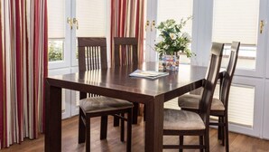 A dining area with a wooden table and chairs, a vase with flowers, and striped curtains. - Gemütlich. Komfortabel. Wellness. Residenz Bismarck, Whg. 6 Objekt-id: Hrb/06 (Westerland)