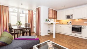 A modern kitchen with white cabinets, a microwave, and an oven. There is a dining area with a table and chairs, and a sofa with colorful cushions. - Gemütlich. Komfortabel. Wellness. Residenz Bismarck, Whg. 6 Objekt-id: Hrb/06 (Westerland)