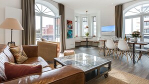 A modern living room with a leather sofa, a glass coffee table, and a dining area with white chairs and a table. - Ausblick. Komfortabel. Südbalkon (Westerland)