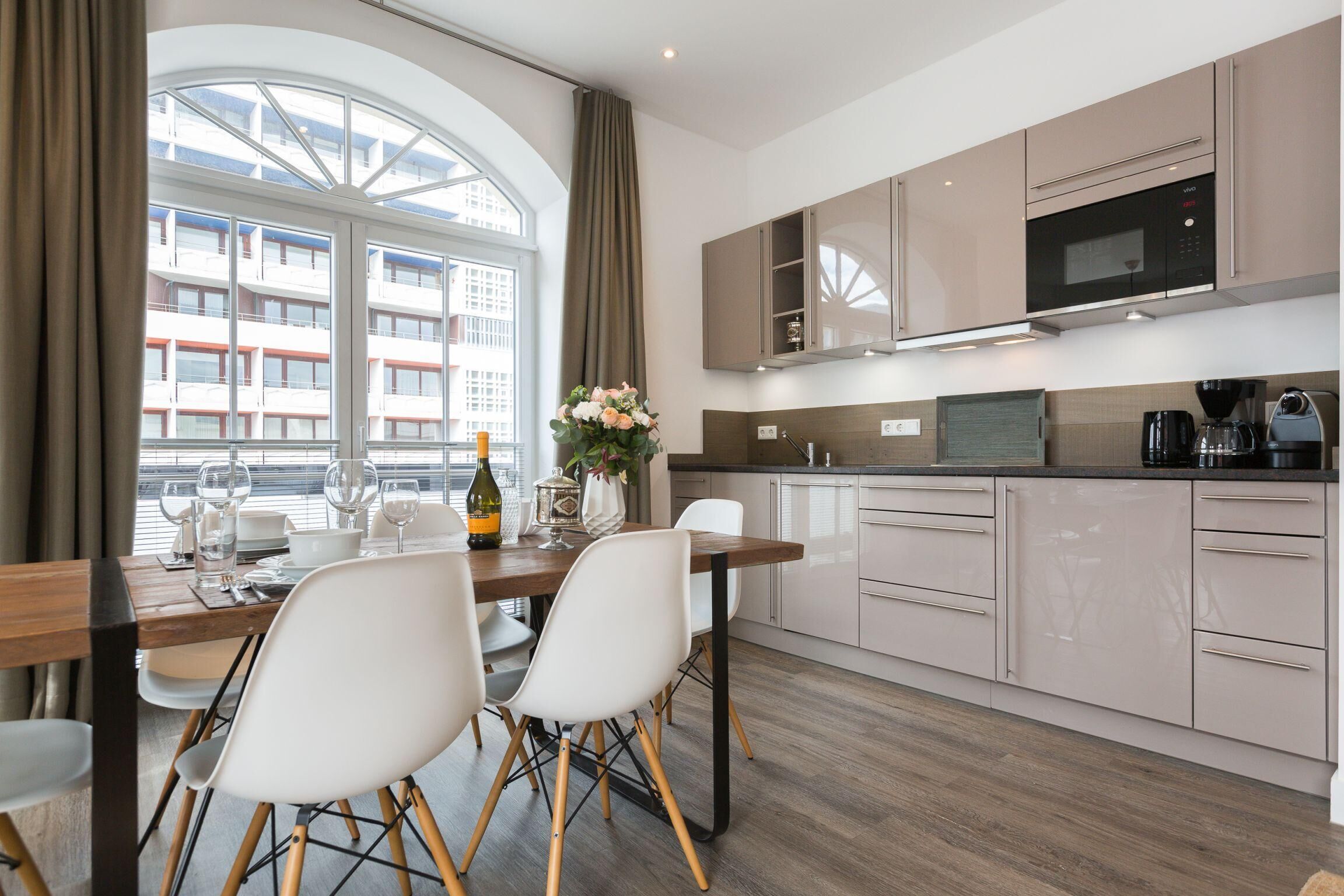 Une cuisine moderne avec un coin repas, de grandes fenêtres et une vue sur les immeubles.