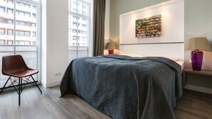 A modern bedroom with a large bed, a chair, a nightstand with lamps, and a wall art piece. - Ausblick. Komfortabel. Südbalkon (Westerland)