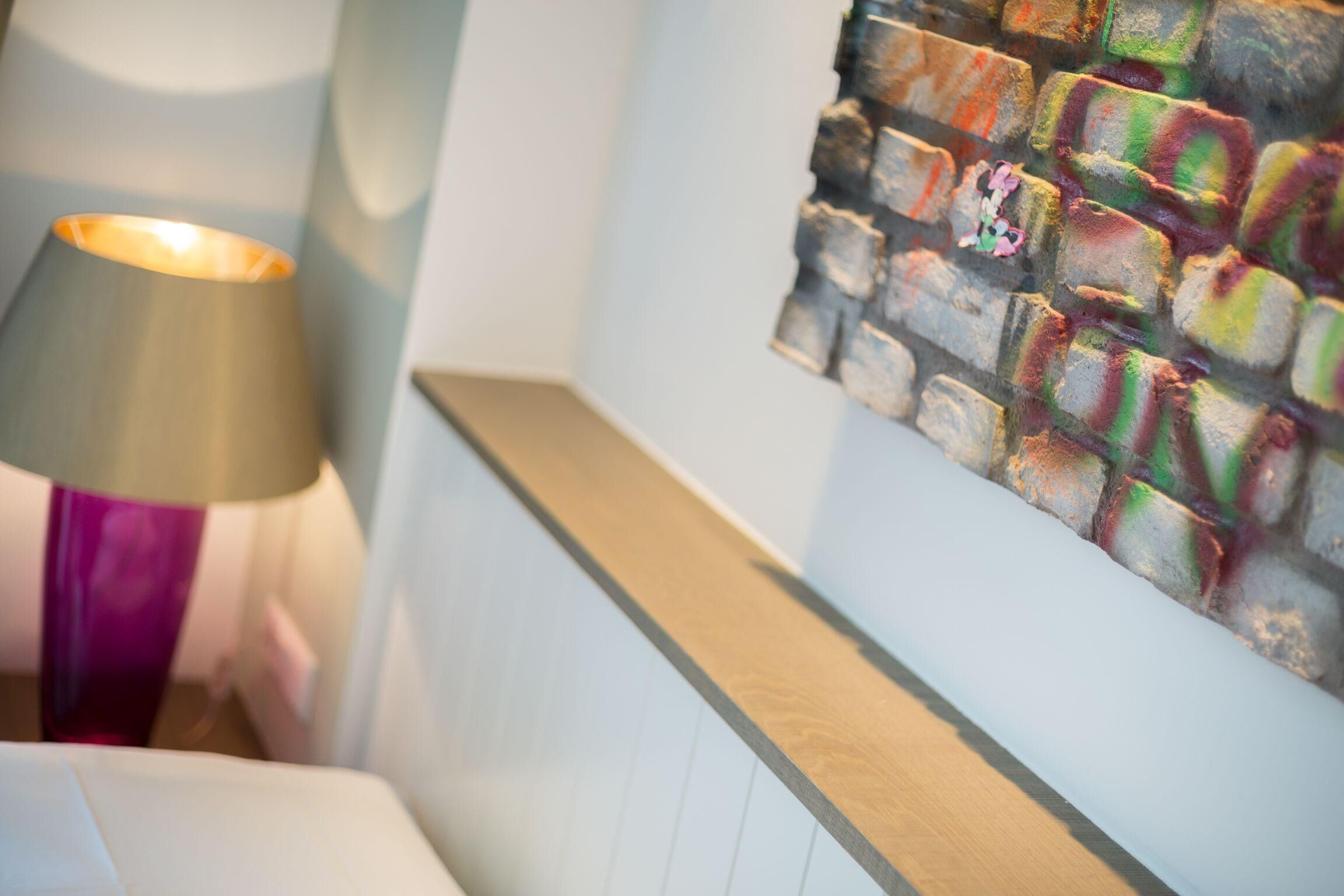 A room with a bed, a lamp, and a colorful abstract wall art.