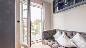 A room with a grey sofa, a wooden table, and a sliding glass door leading to an outdoor deck. - Sonnenfreisitz. Geschmackvoll. Exklusiv (Westerland)
