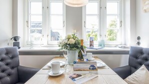 A dining area with a wooden table set for two, a vase with flowers, and a brochure on the table. - Sonnenfreisitz. Geschmackvoll. Exklusiv (Westerland)