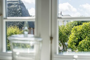 A view through a window with a clear glass vase in the foreground, a brick building, and a tree with green foliage. - Sonnenfreisitz. Geschmackvoll. Exklusiv (Westerland)