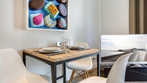 A modern dining area with a wooden table, white chairs, and a view of a beach through a window. - Art your Life - Residence, Whg. 8 Tom (Westerland)