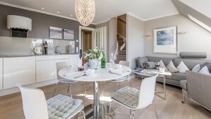 Eine moderne Küche mit weißen Schränken, ein Essbereich mit einem runden Tisch und ein graues Sofa in einem großzügigen Wohnzimmer.