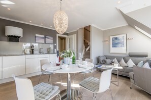 Una cocina moderna con armarios blancos, una zona de comedor con una mesa redonda y un sofá gris en un amplio salón.