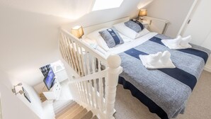 Ein Schlafzimmer mit Bett, zwei Nachttischlampen, einem Fenster und einer Treppe.