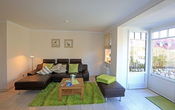 A modern living room with a sectional sofa, a coffee table, and a view of a garden through large windows.