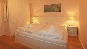 A neatly made bed with towels, a bedside table with a lamp, and a wardrobe. - Exklusiv. Modern. Zentral. Haus Nordmarkgarten, Whg. 7a Objekt-id: Hng/07a (Westerland)