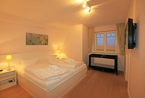 A hotel room with a bed, bedside lamps, a TV, a window with curtains, and a painting on the wall.