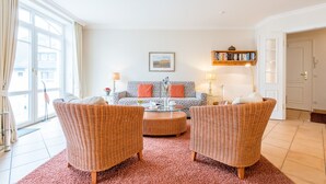 A living room with wicker furniture, a patterned sofa, a coffee table, and a bookshelf.