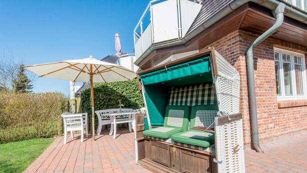 A patio area with a table and chairs, a covered seating area with cushions, and a large umbrella. - Komfortabel. Strandnah. Zentral. Objekt-id: Has/09 (Westerland)
