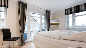 A bedroom with a bed, a chair, a window, and a view of the outside. - Modern. Lichtdurchflutet. Wellness (Westerland)