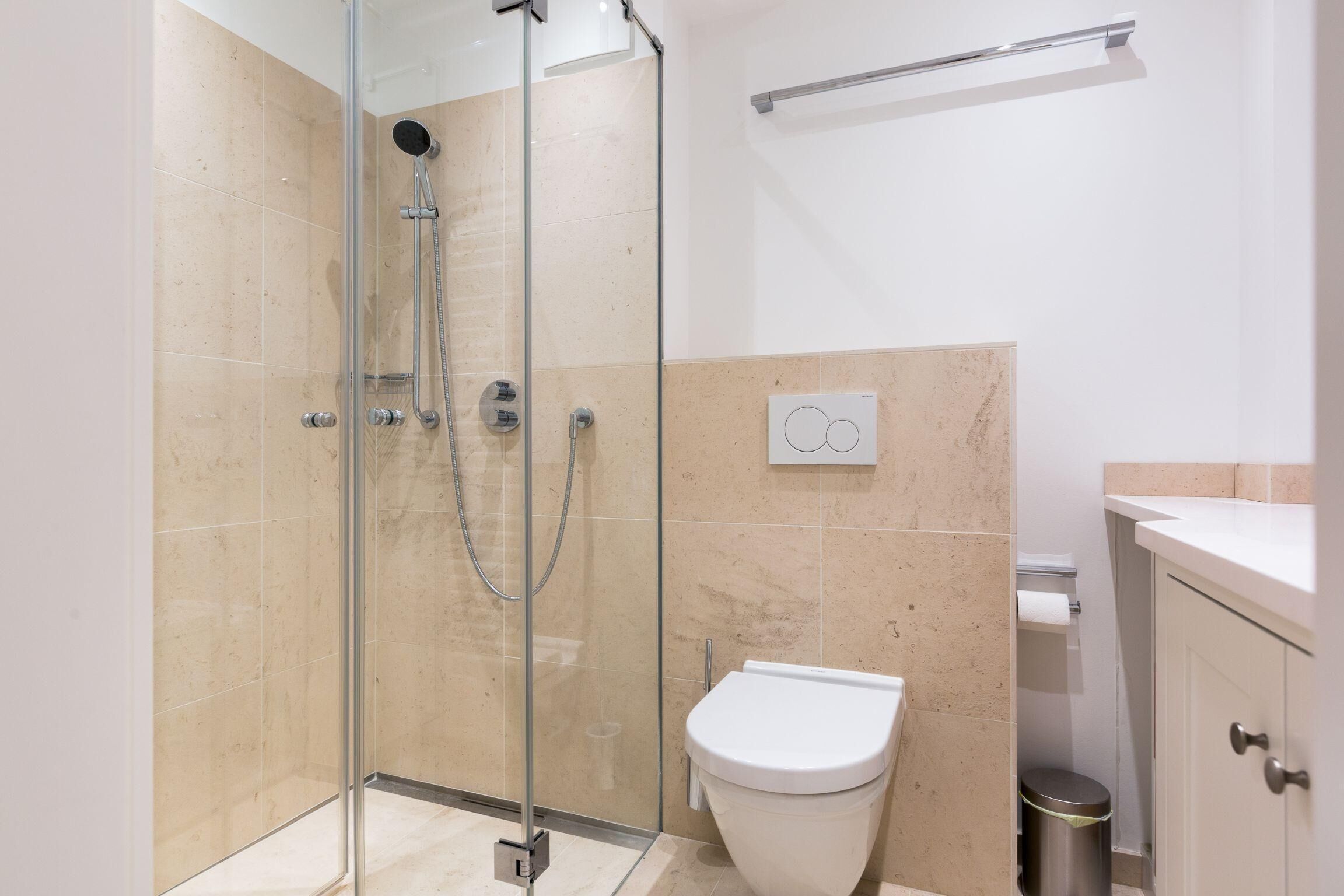 Ein modernes Badezimmer mit einer Glaskabine zur Dusche, einer weißen Toilette und einer kleinen Mülltonne.
