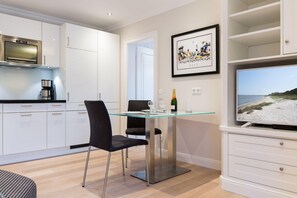A modern kitchen with white cabinets, a stainless steel oven, and a glass dining table with two chairs.