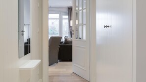 A hallway with a white door, a mirror, and a view into a living area with a sofa and curtains. - Modern. Lichtdurchflutet. Wellness (Westerland)