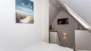 Une chambre à coucher avec un puits de lumière, un tableau représentant un paysage et une table de chevet.