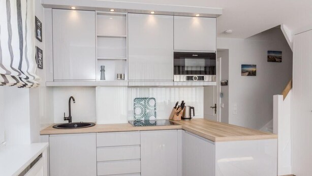 Une cuisine moderne avec des meubles blancs, un plan de travail en bois et un four encastré.