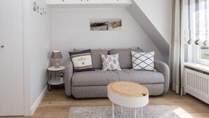 Un salon moderne avec un canapé gris, une petite table d’appoint avec une lampe, une table basse ronde et un tableau au mur.