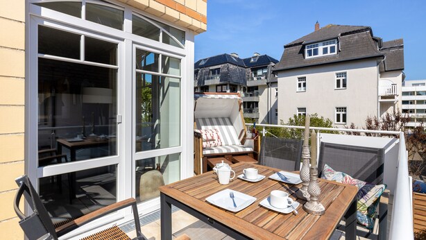 Eine Terrasse im Freien mit einem Holztisch, gedecktem Esstisch, einer gepolsterten Sitzecke und Blick auf umliegende Gebäude.