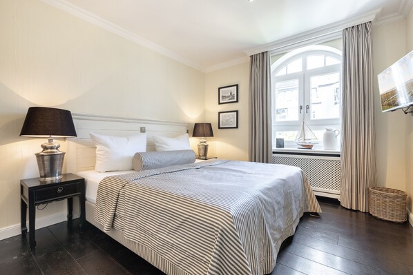 Une chambre d’hôtel avec un grand lit, deux tables de chevet avec des lampes, une fenêtre avec des rideaux et un téléviseur fixé au mur.
