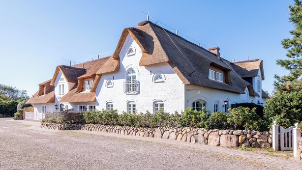 A large white building with a steeply pitched roof, multiple windows, and a stone wall in front. - Hyggelig. Reet. Wellness. "dansk Hygge" im Witthüs, Whg. 10 Objekt-id: Wiw/10 (Wenningstedt)