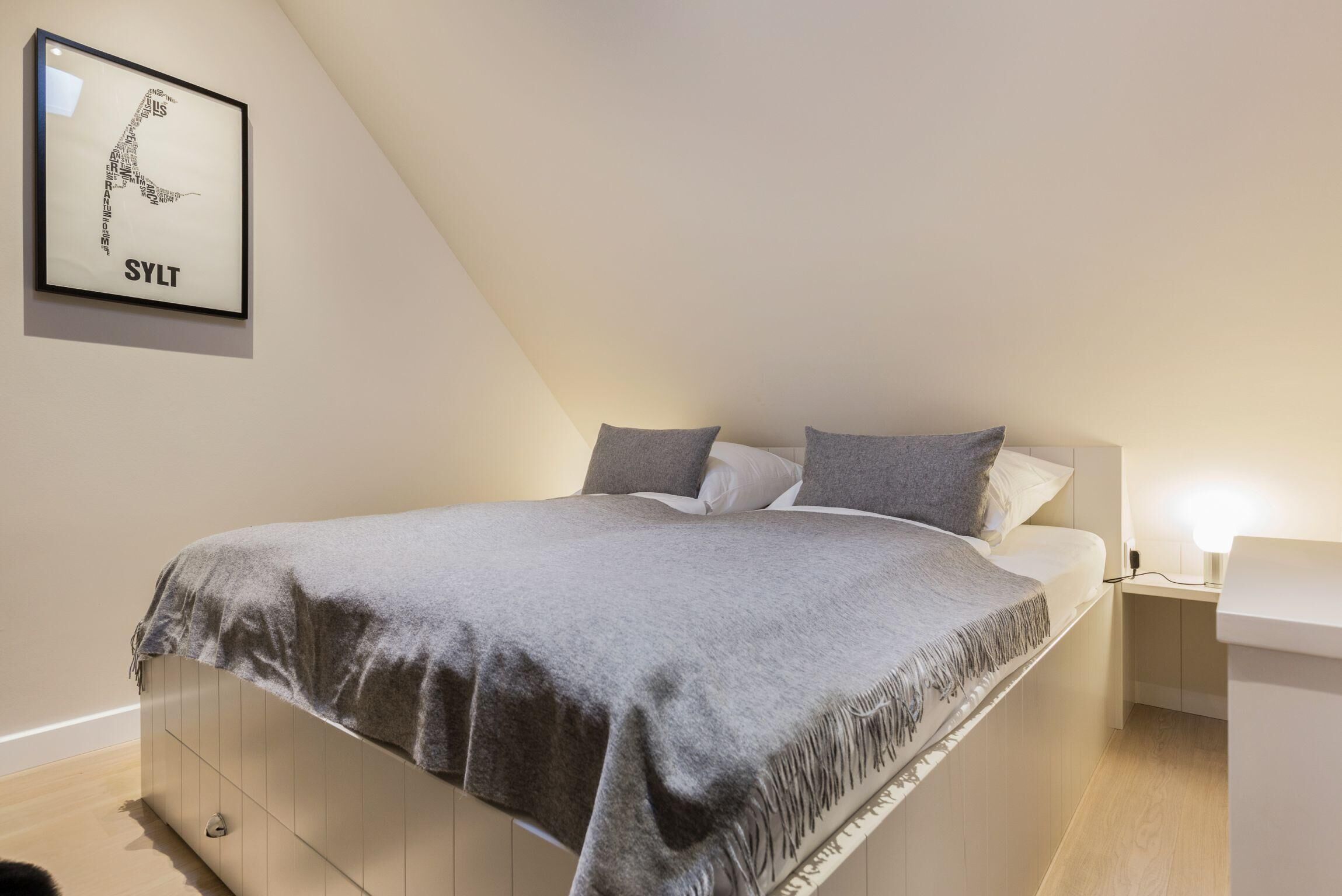 A bedroom with a bed, pillows, a bedside table, and a wall-mounted picture.