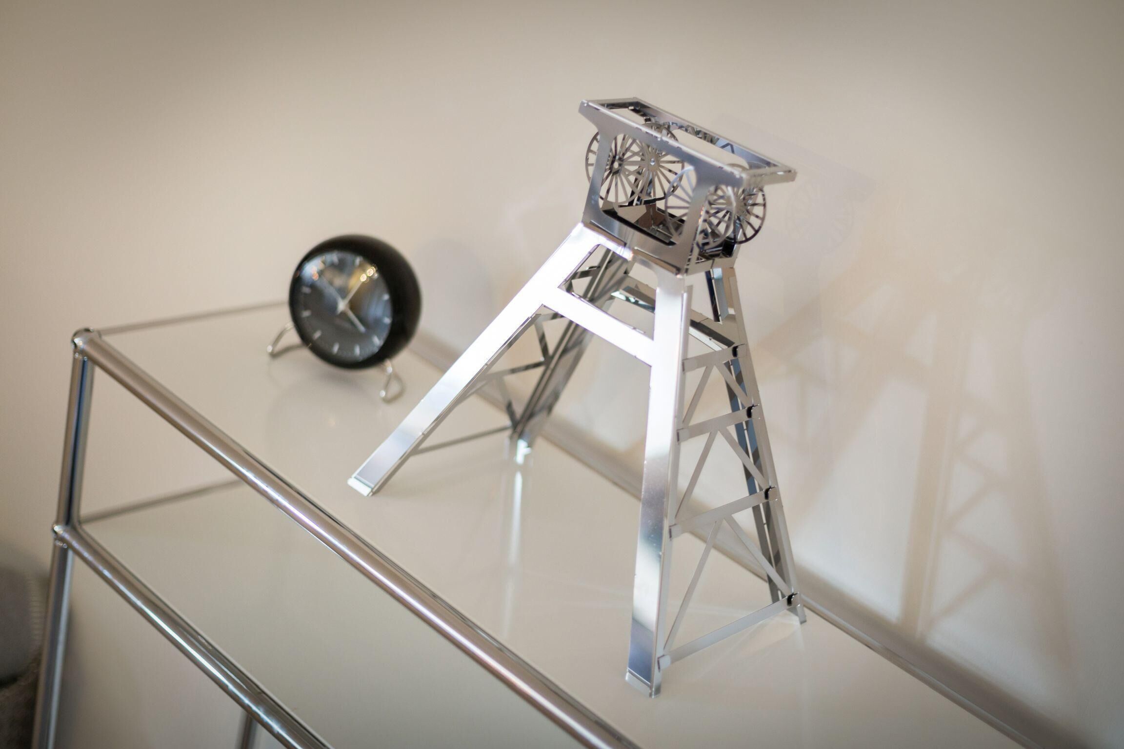 A metallic stand with a reflective surface and a clock on a glass table.