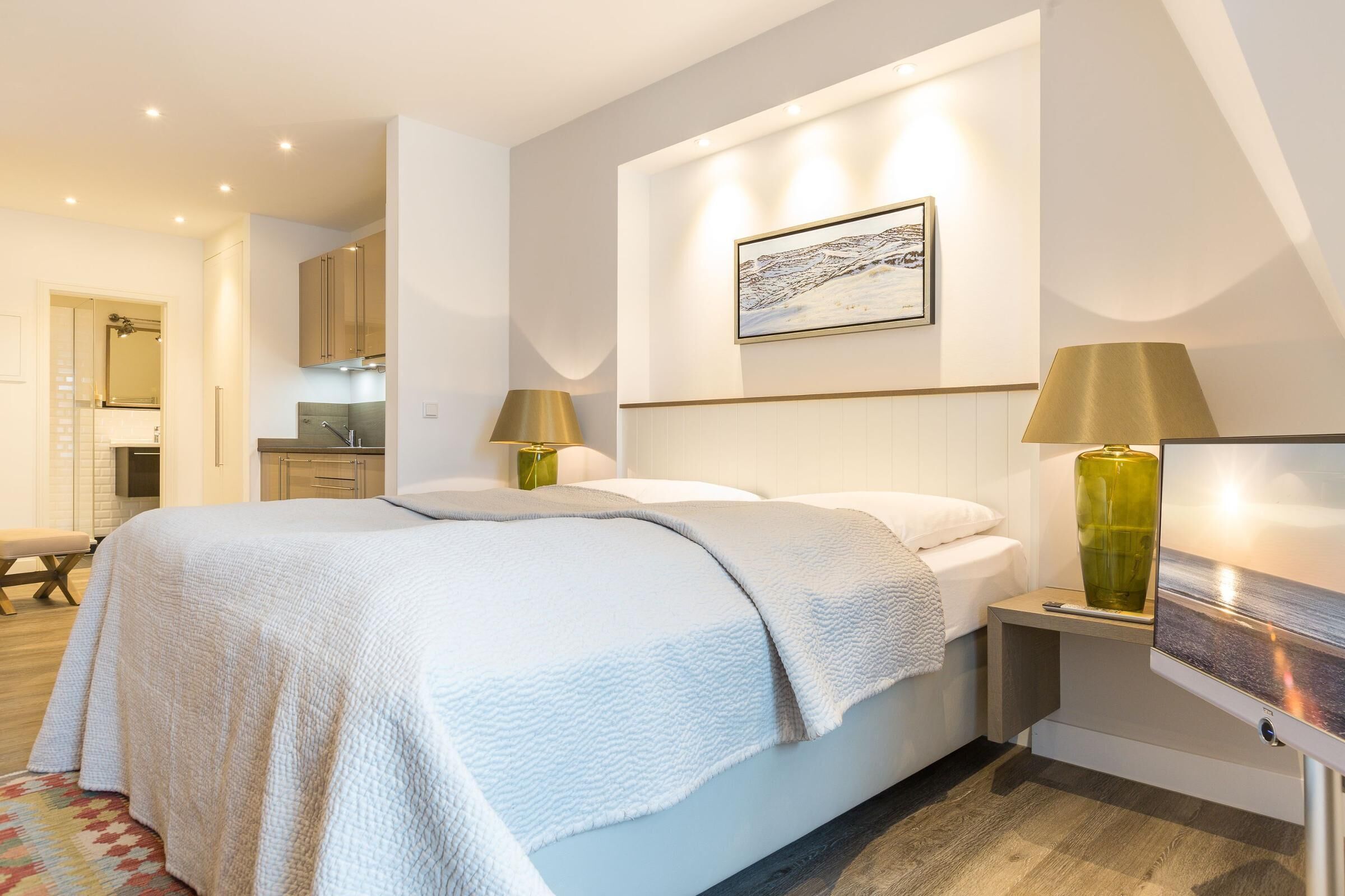 Een slaapkamer met een bed, bedlampen, een schilderij en een klein tafeltje met een vaas.
