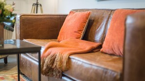 Ein braunes Ledersofa mit orangefarbenen Kissen und einer Decke.