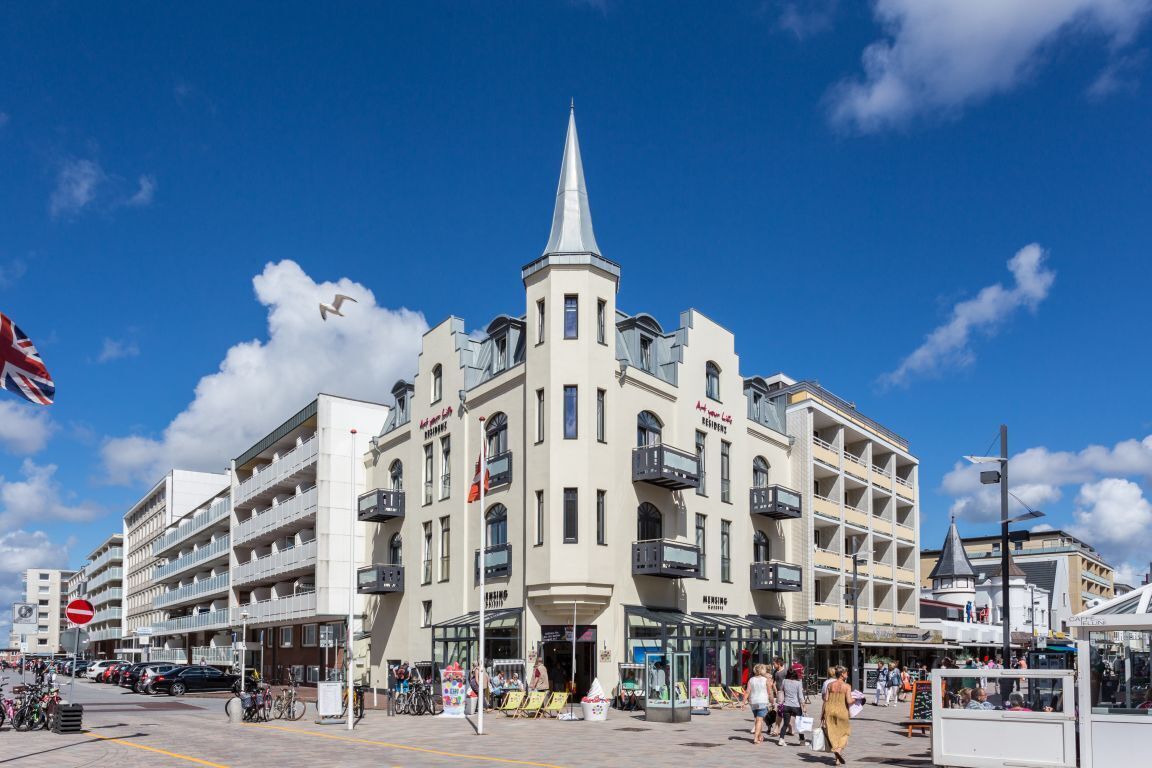 Een hotel met meerdere verdiepingen, balkons, een centrale toren en een entree op de begane grond.