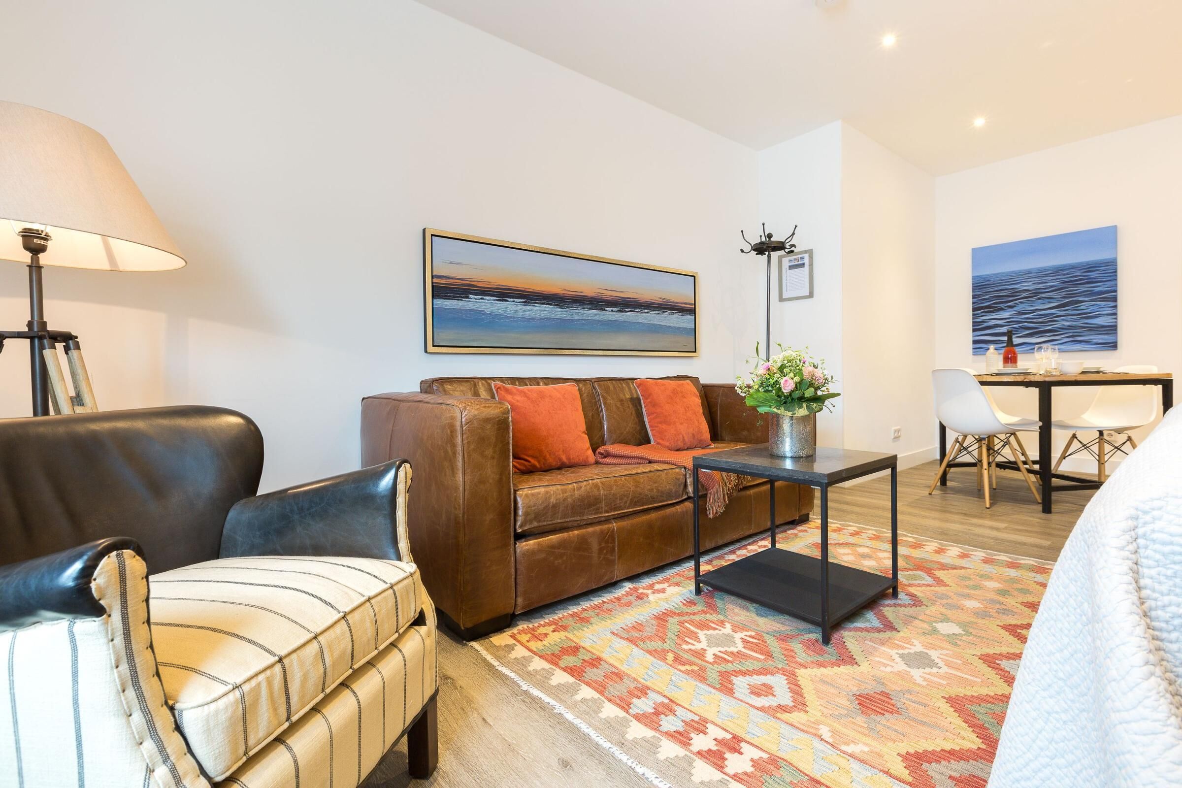 Een woonkamer met een bruine leren bank, een gestreept fauteuil, een salontafel en een vloerkleed.