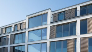 En modern byggnad med flera våningar, stora fönster och träribbor på de övre våningarna.