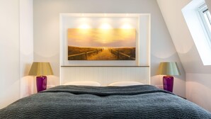 A bedroom with a large bed, a painting of a sunset over a beach, and two lamps on either side. - Großzügig. Ausblick. Wellness (Westerland)