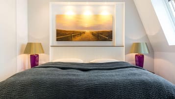 Un dormitorio con una cama grande, un cuadro de un atardecer sobre una playa y dos lámparas a cada lado.
