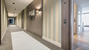 A long, narrow hallway with a carpeted floor, wooden panel walls, and a door marked with the number 12.
