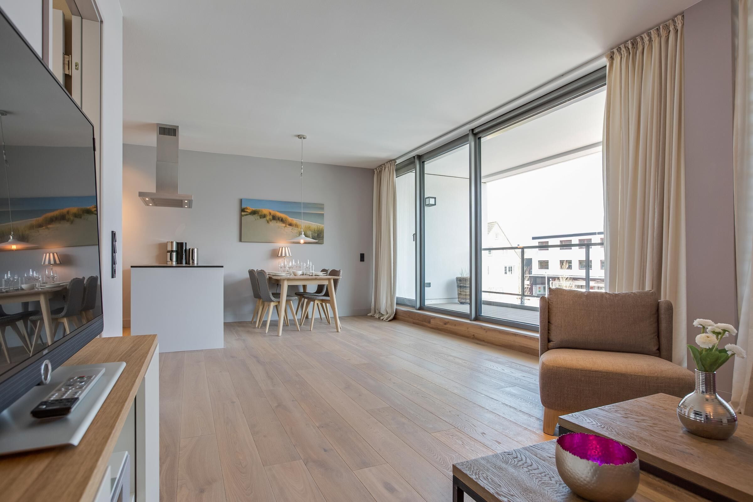 A modern living room with a large window, a dining area, and a kitchen.