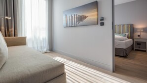 A modern hotel room with a large bed, a bedside table, a nightstand, a lamp, and a painting on the wall.