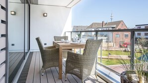 A balcony with wicker chairs, a wooden table, and a view of buildings and a tower.