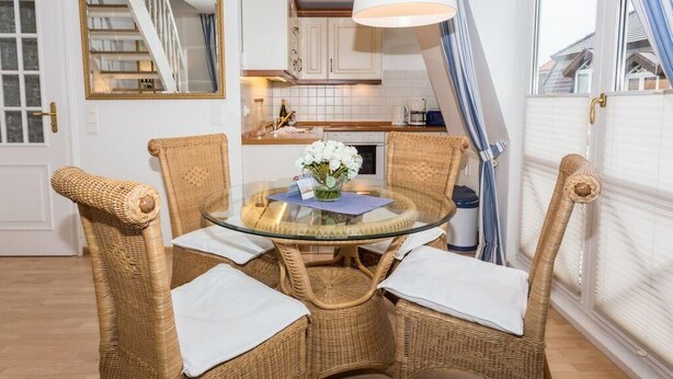 A dining area with wicker chairs, a glass table, and a vase of flowers.
