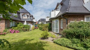 A residential area with houses, a well-maintained lawn, and various shrubs and flowers.
